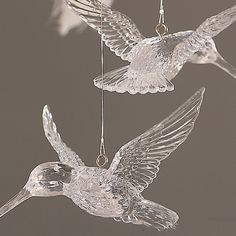 two clear glass birds hanging from strings on a gray background, one flying and the other hovering