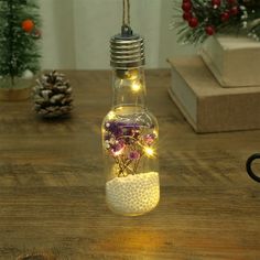 a light bulb filled with flowers sitting on top of a wooden table next to a christmas tree