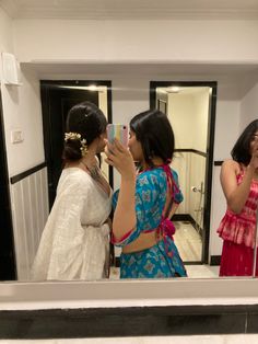 three women are standing in front of a mirror and taking pictures with their cell phones