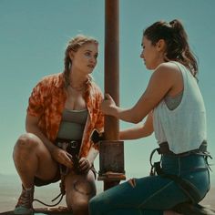 two women sitting next to each other near a pole