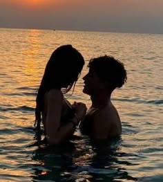 two people in the water at sunset, one is kissing the other's head