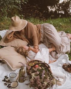 two women laying on a blanket in the grass next to some flowers and other items