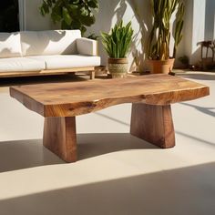 a wooden table sitting on top of a white floor next to a couch and potted plants