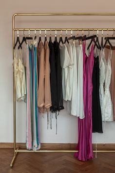 a rack with clothes hanging on it in front of a white wall and wooden floor