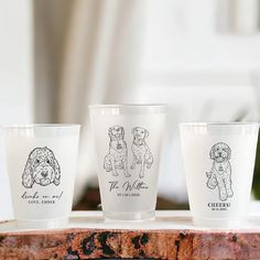 three shot glasses with dogs on them sitting on a wooden table in front of a window