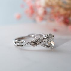 a close up of a diamond ring on a white surface with flowers in the background