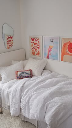 a white bed sitting in a bedroom next to two pictures on the wall above it