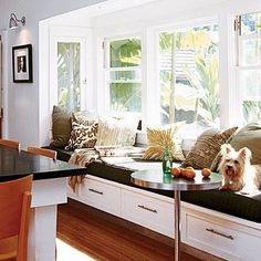 a dog sitting on a window seat in a living room next to a table and chairs