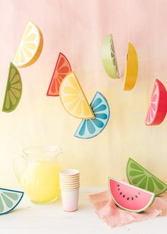 a table topped with plates and cups next to a pitcher filled with oranges, watermelon slices