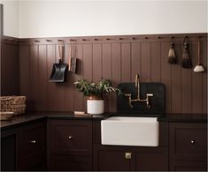 a kitchen with wooden paneling and black counter tops has a white sink, brass faucet, and hanging utensils on the wall