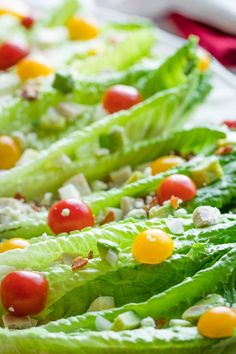 lettuce with tomatoes, cheese and other toppings sitting on a white plate