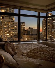 an unmade bed in front of a large window with the city lights out at night