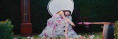 a woman in a dress is sitting on a lawn chair with pink flowers around her