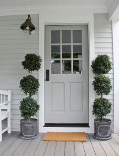 two potted plants are on the front porch next to a white door that says happy