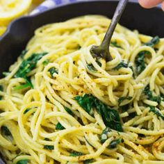 someone is holding a fork in a bowl of pasta with spinach and lemons