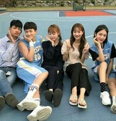 group of young people sitting on top of a basketball court posing for the camera with their thumbs up