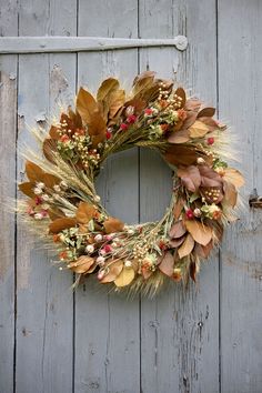 a wreath is hanging on the side of a wooden door with dried leaves and berries