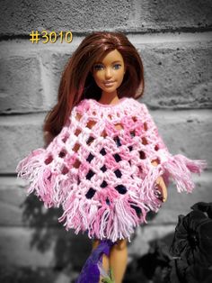 a doll wearing a pink crocheted ponchy with fringes on it