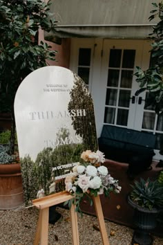 a white grave marker with flowers on it in front of a house and potted plants