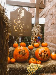 pumpkins are stacked on top of hay in front of the salem witch museum sign