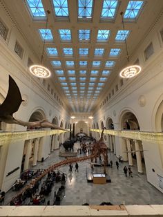 an indoor museum filled with lots of people and dinosaur skeletons in the middle of it