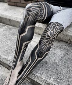 a person with black and white tattoos on their legs sitting on some steps, wearing leggings