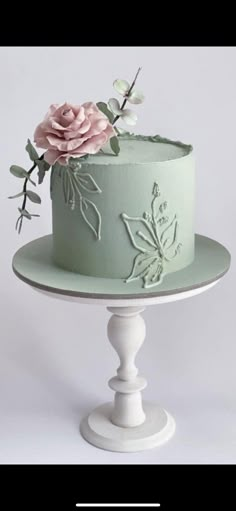 there is a green cake with flowers on the top and bottom tier, sitting on a white pedestal