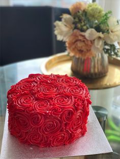 a red cake sitting on top of a table next to a vase filled with flowers