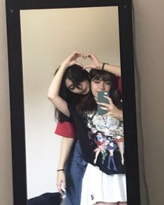 two young women standing in front of a mirror making a heart shape with their hands