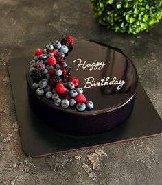 a chocolate birthday cake with berries and blueberries on the top is sitting on a black plate