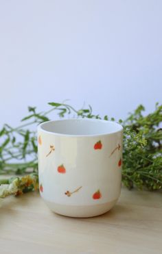 a white cup sitting on top of a wooden table next to green leaves and flowers