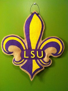 the lsu logo is hanging on the wall in front of a green background with yellow and purple fleurons