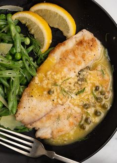 a plate with fish, asparagus and lemon wedges on it next to a fork