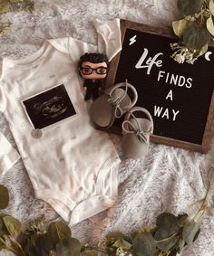 a baby's bodysuit and shoes are laid out next to a sign that says, life finds a way