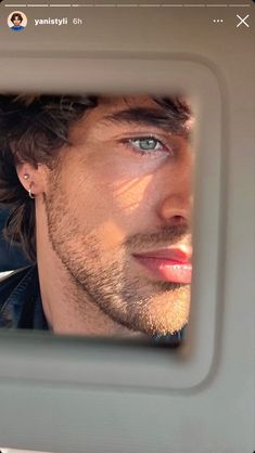 a man with blue eyes looking at himself in the rear seat of a car mirror