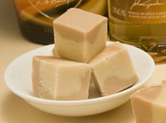 several pieces of fudge sit on a white plate next to two bottles of booze