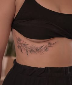 a woman's stomach with flowers and leaves tattooed on her lower back, while wearing a black crop top