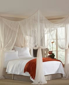 a white bed sitting in a bedroom next to a window with sheer curtains on it