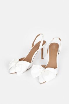 a pair of white high heeled shoes with a bow