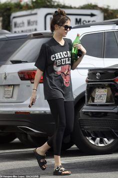 a woman walking across a parking lot holding a green bottle