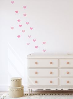 a white dresser sitting next to a wall with pink hearts on it