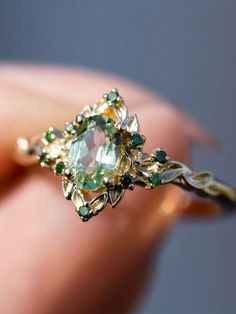 a woman's hand holding an antique ring with green and yellow stones