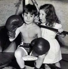 an old photo of two children with boxing gloves on and one holding a punching glove