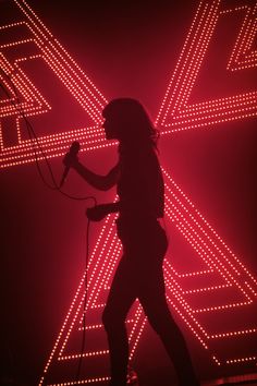 a woman is standing in front of a red light with her hair up and holding a microphone