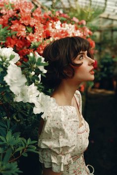 a woman standing in front of flowers with her head tilted to the side and eyes closed