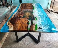 a table made out of wood with blue paint on the top and green trees in the middle