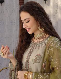 a beautiful woman in a green and gold outfit looking down at her hand while standing next to a wall