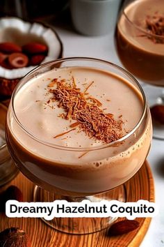 two glasses filled with liquid sitting on top of a wooden plate next to nuts and other food