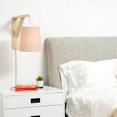 a bed with white sheets and pillows next to a nightstand with a lamp on it