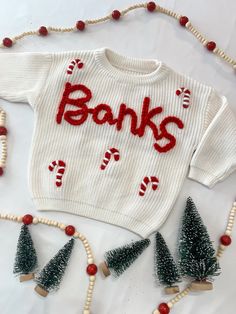 a white sweater with the word banks on it and christmas decorations around it, along with beads